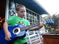 IMGP0568  Sam playing his new guitar - Daddy came home with a new drum set and a new guitar as a big surprise! Sam has been playing drums for about 18 months on second-hand drums from his friends. One of the sets made it all the way across the island to Goodwill where I hunted it down by phone and had them hold it for mom who grabbed it for Sam! So now we have three drums sets, only one of which we've purchases. The second-hand ones are very very worn, though, and too rickety to stay together. Ben's set has only one intact side, the other is blown out, but he doesn't mind a bit :)